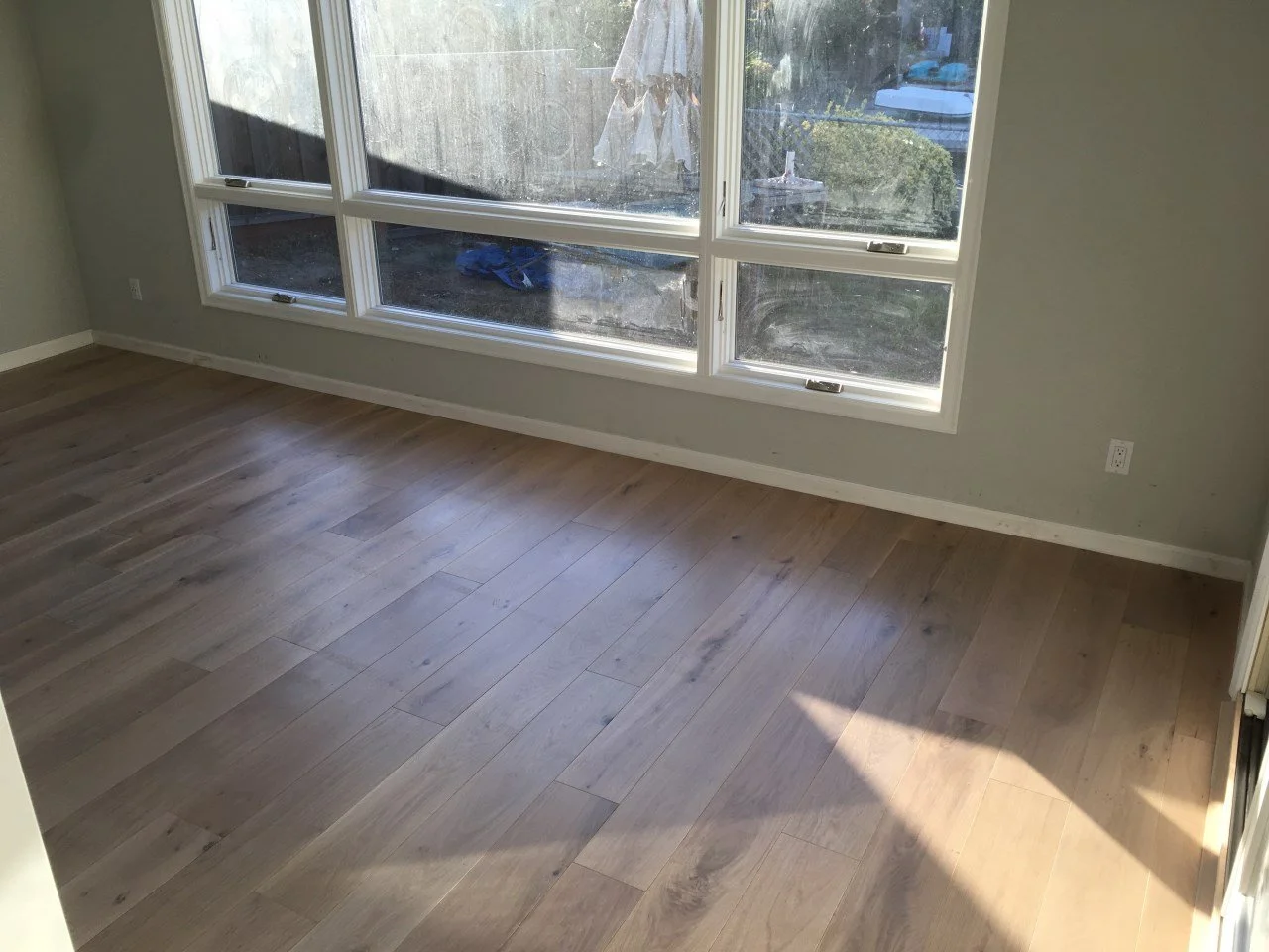 Completed bedroom with new wide plank flooring and large windows bringing natural light into the remodeled Alameda waterfront home.
