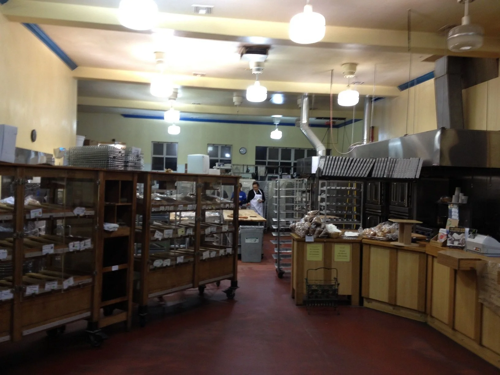 View from the front of the bakery looking toward the production area, highlighting open shelving, warm lighting, and the visual connection between customer space and baking operations.