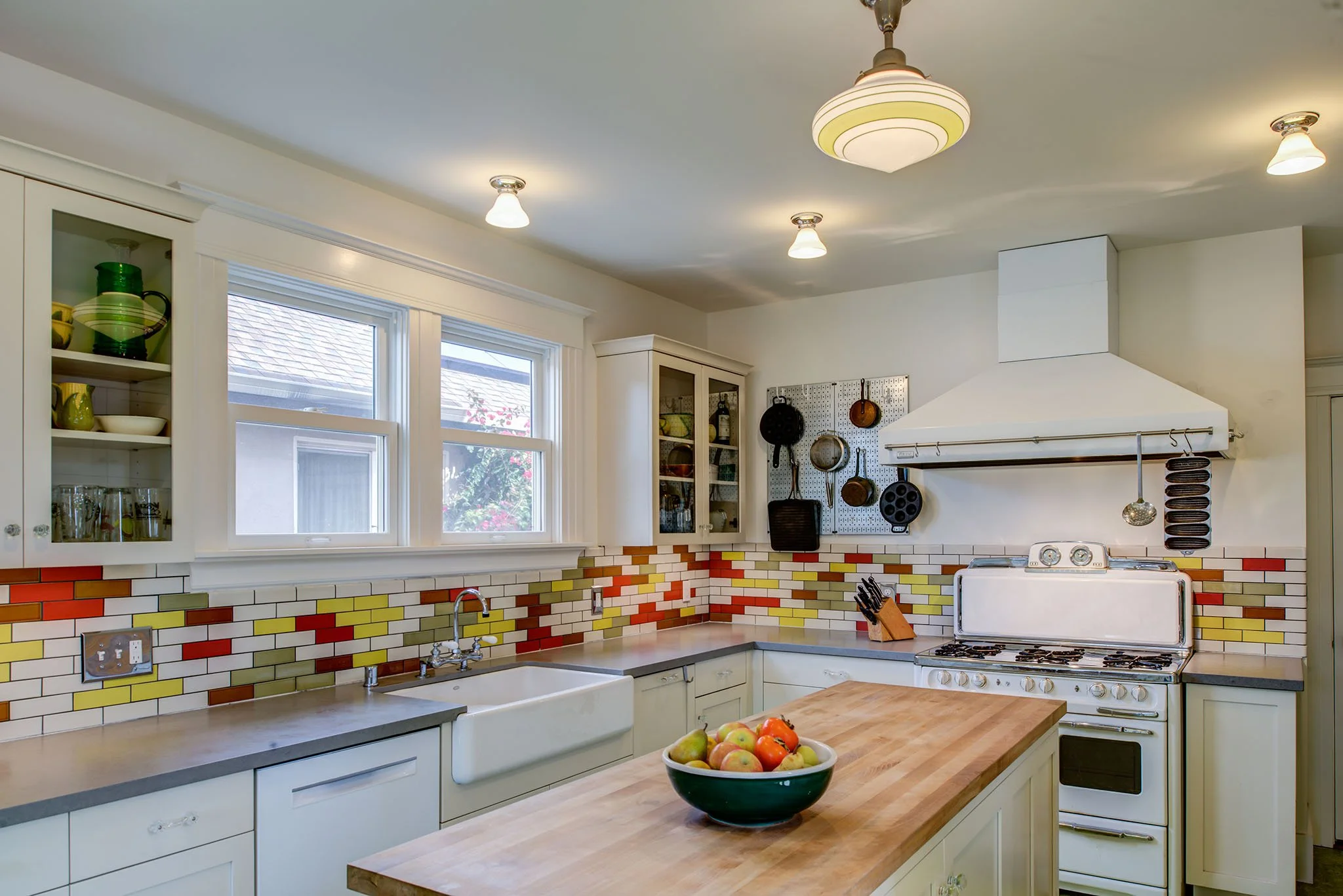 Updated Craftsman kitchen with butcher block island, farmhouse sink, colorful tile backsplash, and vintage style range and hood, adding function with eclectic color.