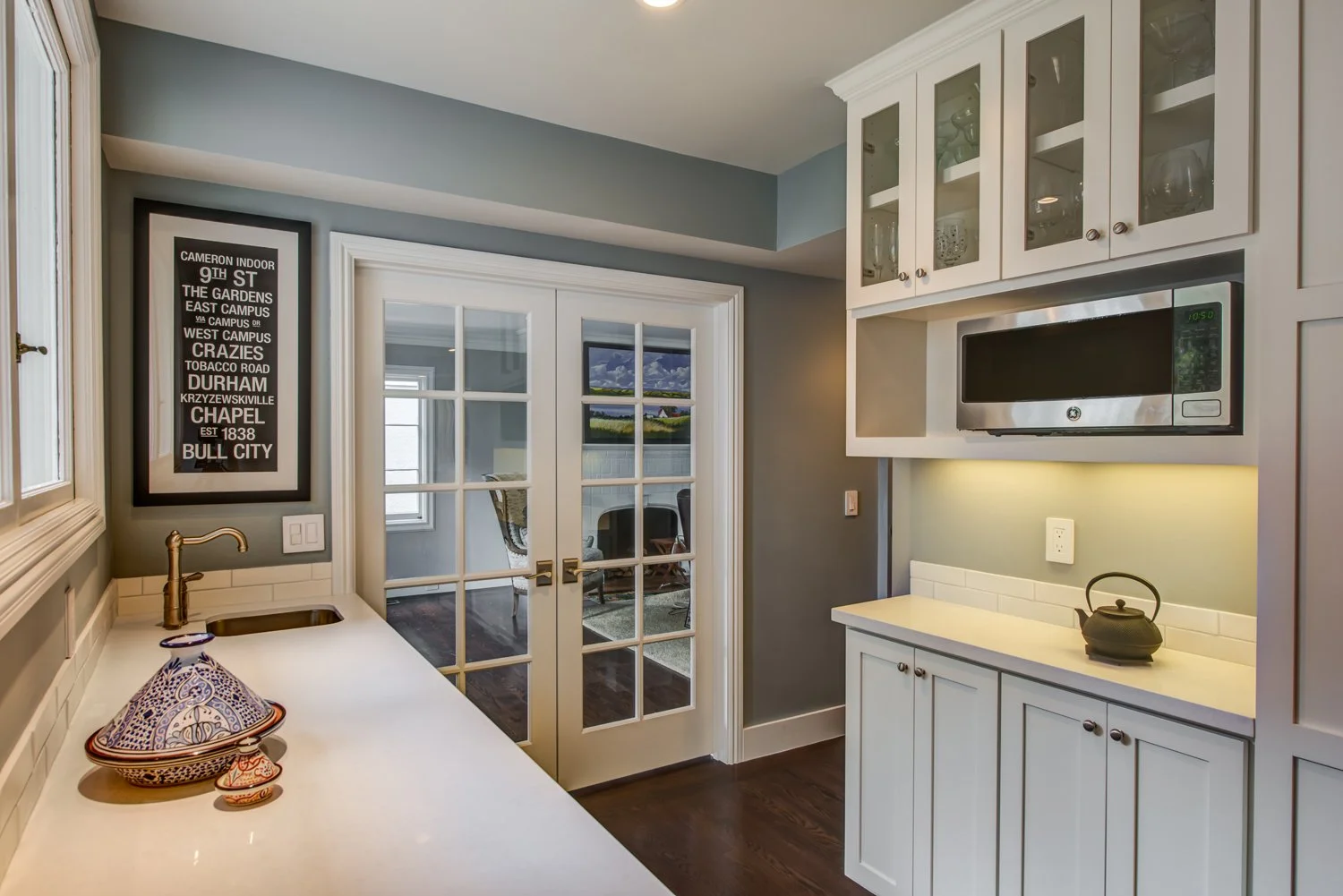 Separate buffet counter area in the remodeled kitchen with glass cabinets, a small prep sink, and French doors, adding storage and serving space for gatherings.