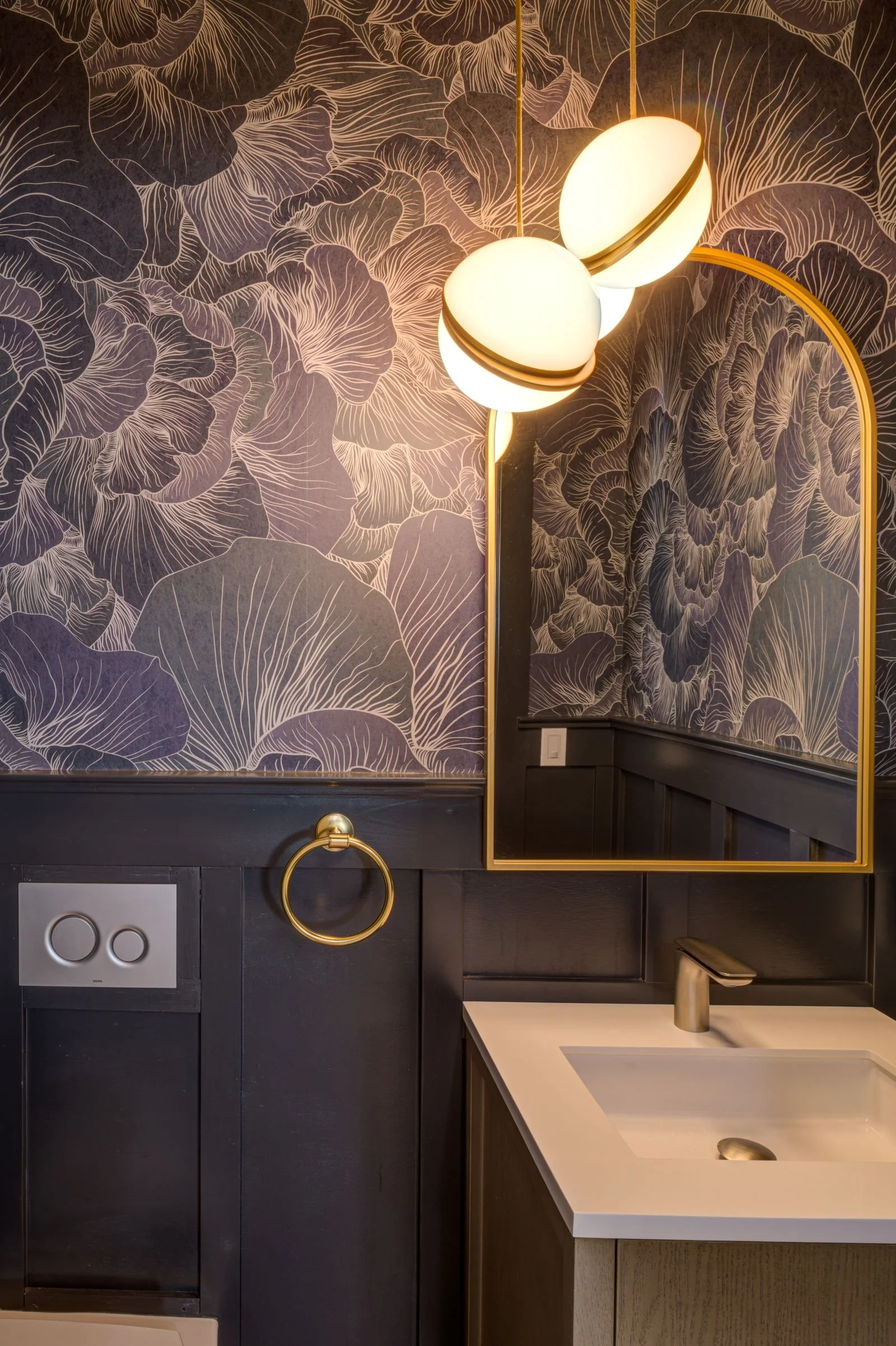 New Main Floor Powder Room with navy blue wainscoting and complementary blue and white floral wallpaper extending from the wainscoting to the ceiling. Frosted glass and brass pendant light fixture over the sink with brass accents repeating in the tow