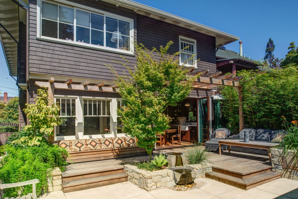 Wide view of the remodeled Craftsman kitchen showing dark wood cabinets, light counters, stainless appliances, and an island that opens to dining and living.