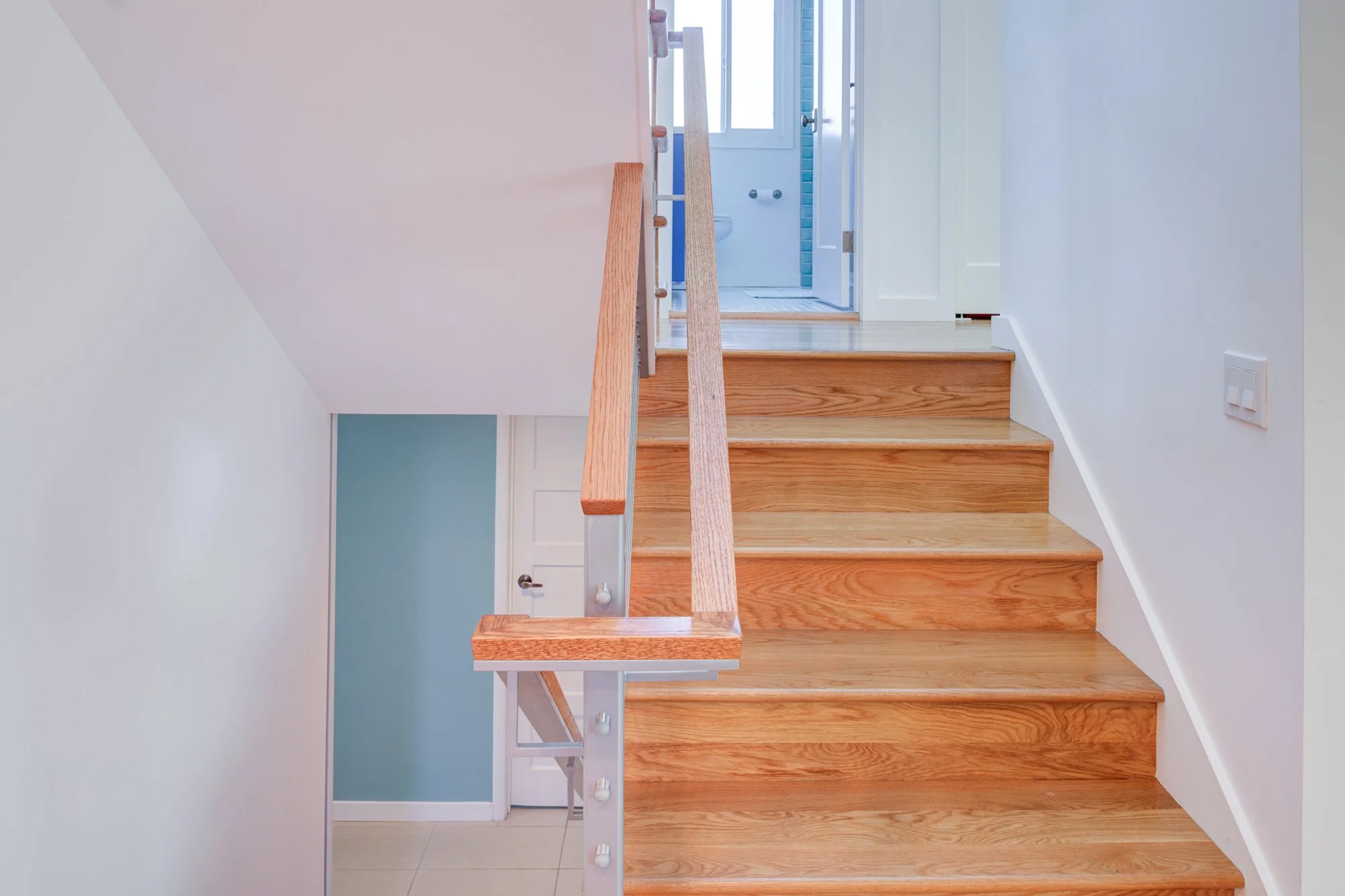 Staircase view showing wood treads and cable railing leading to the second floor, with a bathroom visible beyond as part of the expanded floor plan.