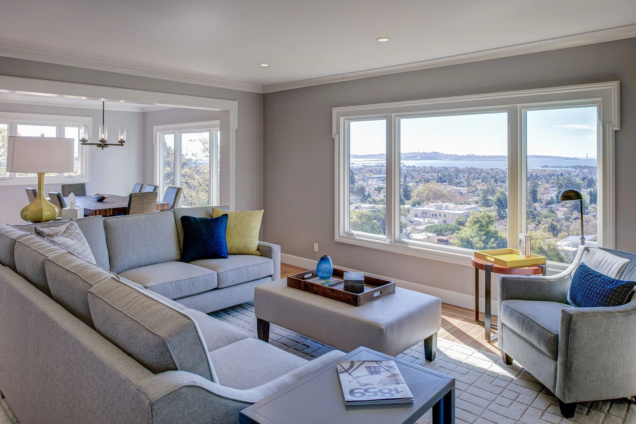 Living room seating arranged to enjoy expansive Bay views through a large picture window. Soft gray walls and clean trim keep the open plan feel light, airy, and connected to the outdoors.