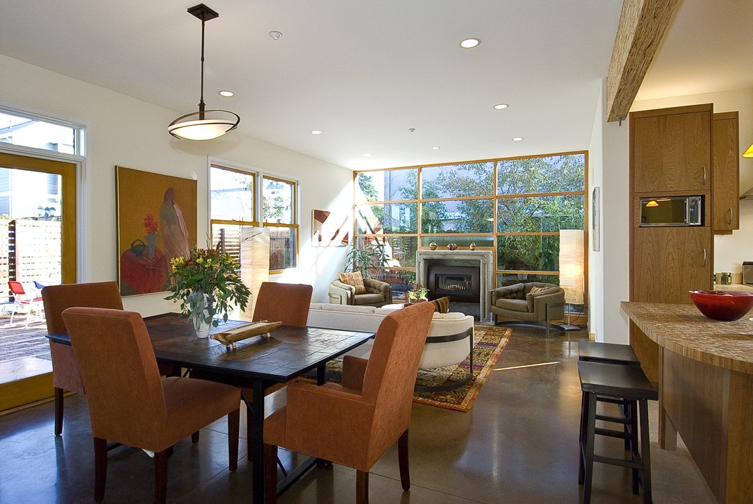 View from dining area toward the living room fireplace, highlighting open circulation, natural materials, and generous glazing used throughout the sustainable new home.