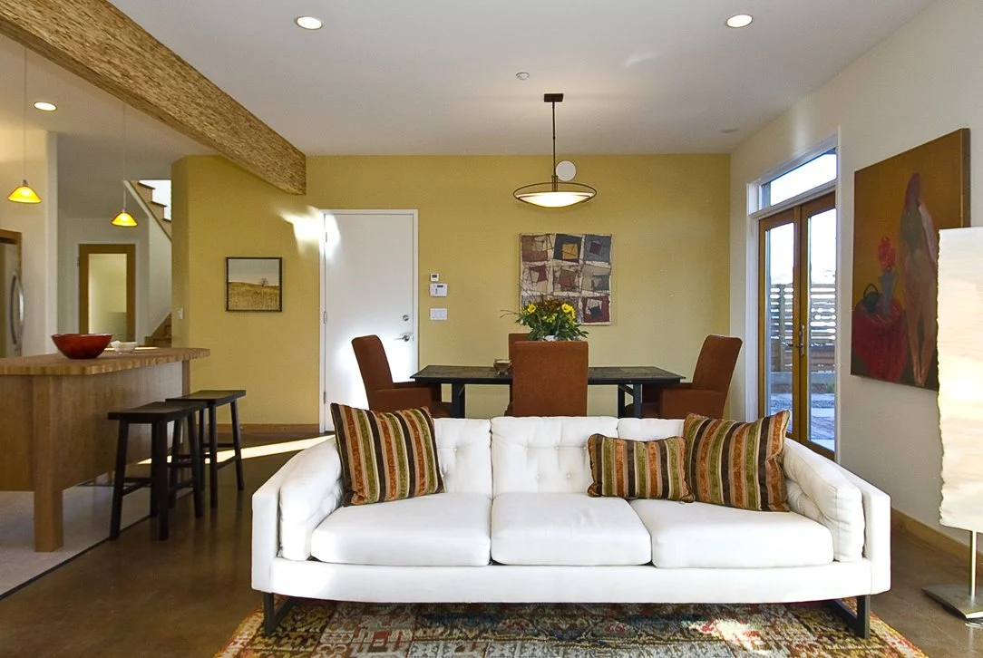 View from living room toward the dining area, showing open circulation, warm material palette, and clear visual connections between shared living spaces.