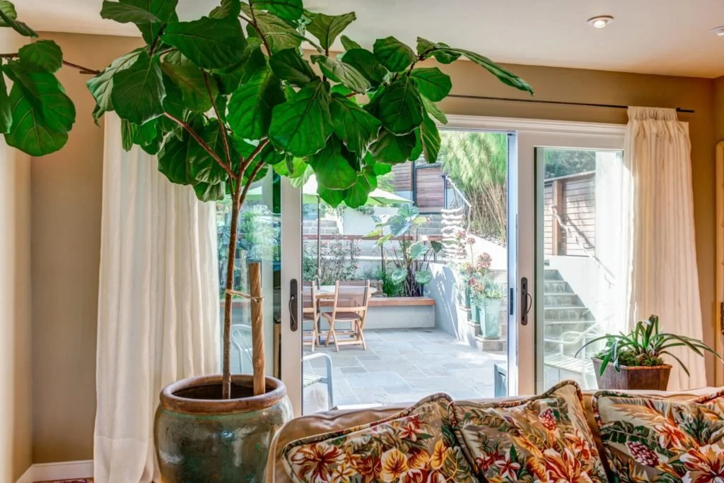 View from the living room through a large sliding door to the new terraced patio, showing Levitch outdoor living spaces on a sloping lot with natural materials and garden planting.