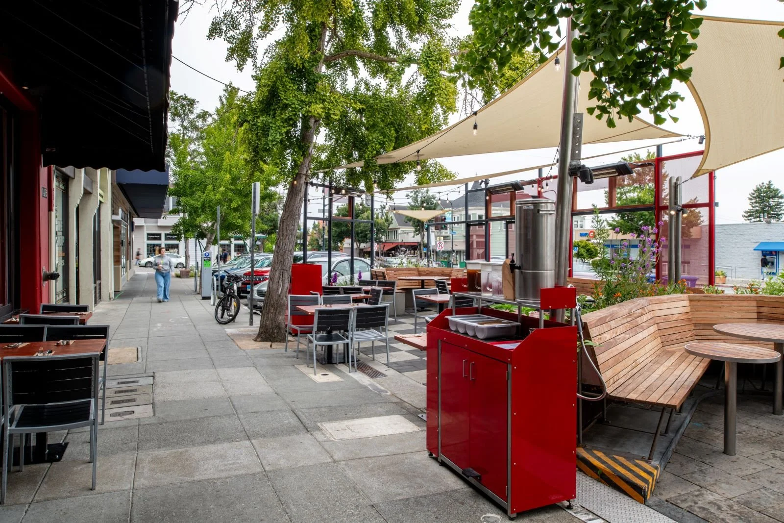 View of sidewalk between the main restaurant building and the parklet. Custom red metal bussing station in the foreground.