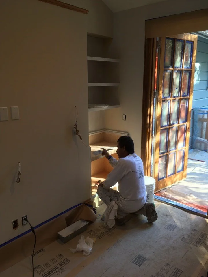 Family room under construction, showing built-in shelving being installed near a glass door that leads to the exterior.