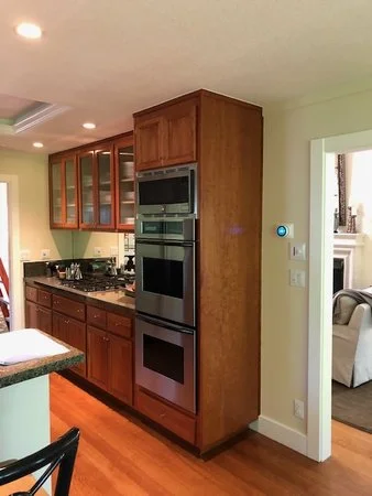 Existing kitchen cooking wall before renovation with dark cabinetry, double wall ovens, and dated finishes later replaced with a lighter, more open design.