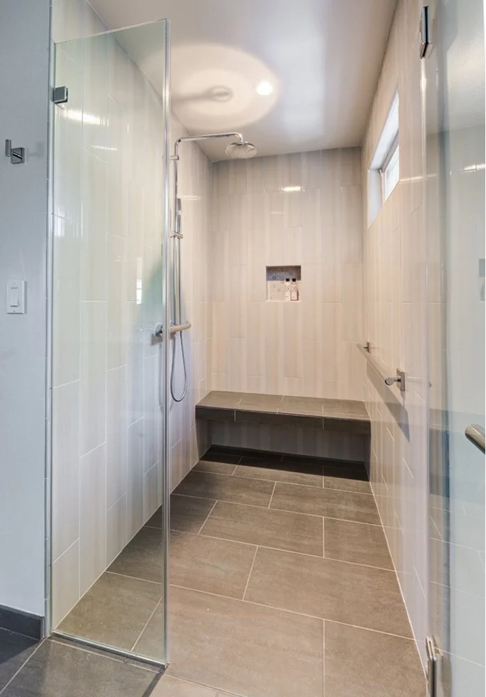 Curbless aging-in-place shower with linear drain below built-in bench, designed for accessibility.