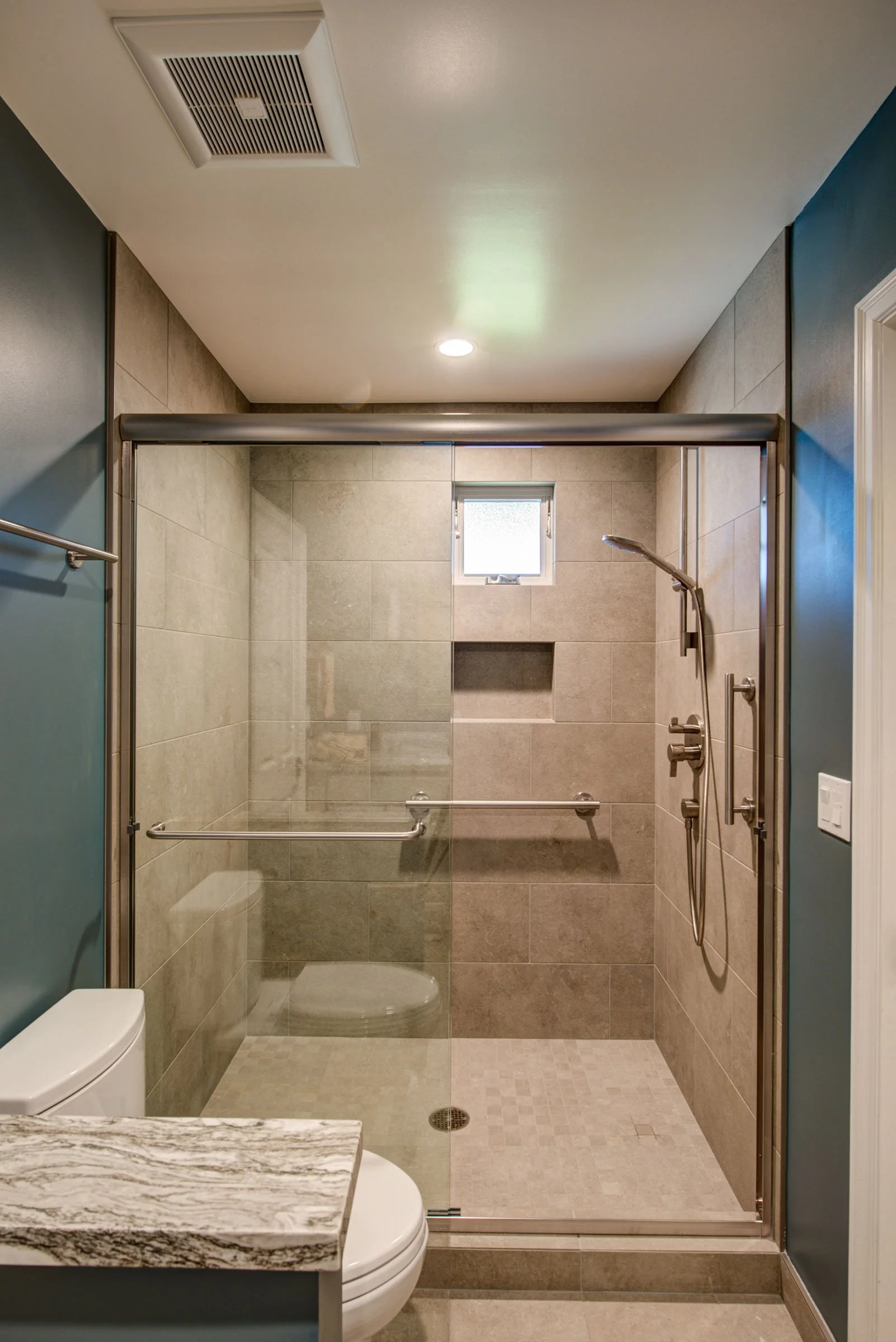 Accessible shower with glass enclosure, built in niche, linear drain, and safety grab bars that support aging in place while maintaining a modern design.