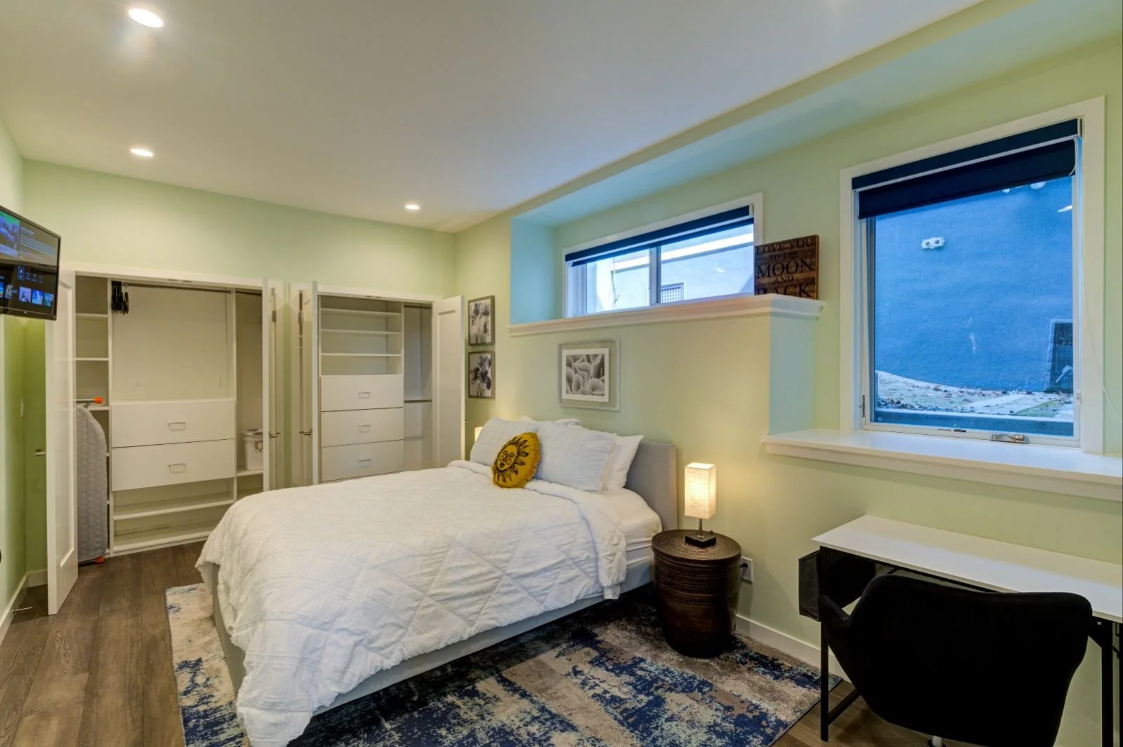 Bedroom in the Grand Lake ADU by Levitch with queen bed, built in closets, desk workspace, soft green walls, recessed lighting, and wide windows for daylight.