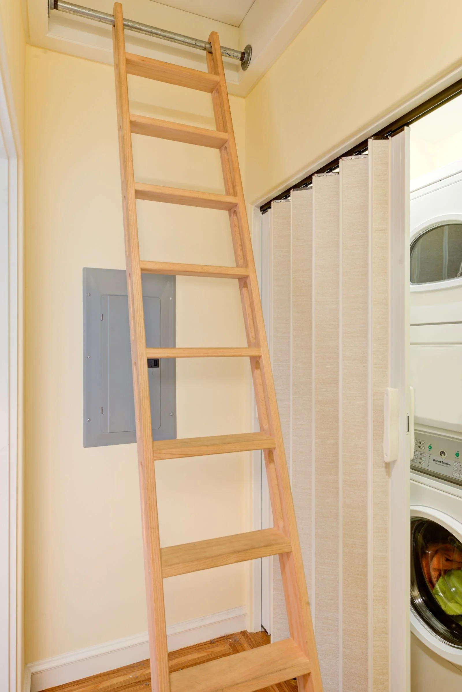 Custom ladder for attic access, with stacked laundry machines behind an accordion door at right.