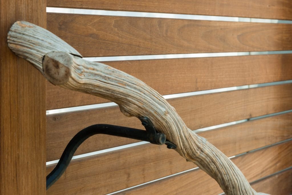 Close detail of the custom branch style handrail mounted to a dark metal bracket on the wood fence, highlighting the natural materials used throughout the project.