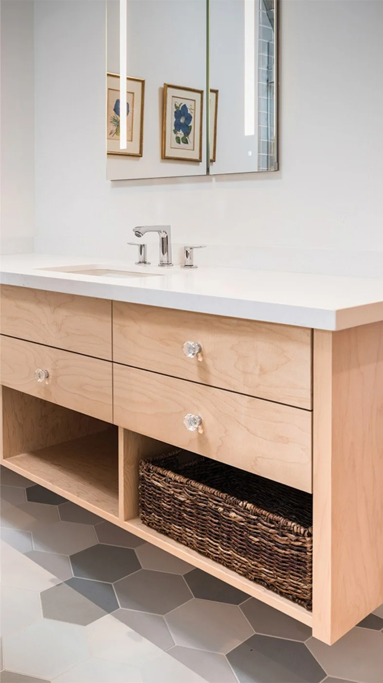 Bathroom vanity with light wood drawers, quartz countertop, and hexagonal tile flooring