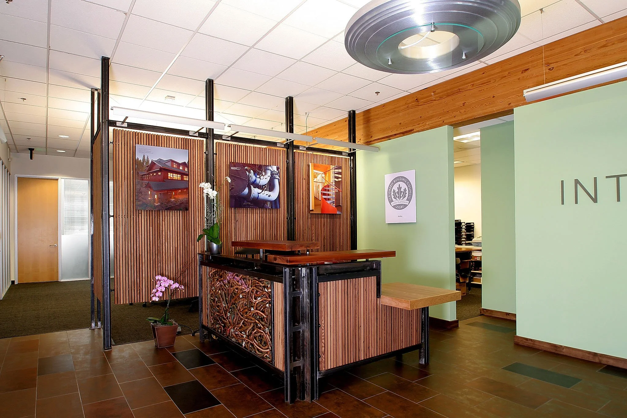 Close view of the recycled material reception desk with steel frame, redwood slats, copper pipe pattern panel, and daylight friendly lighting in the LEED Platinum lobby.