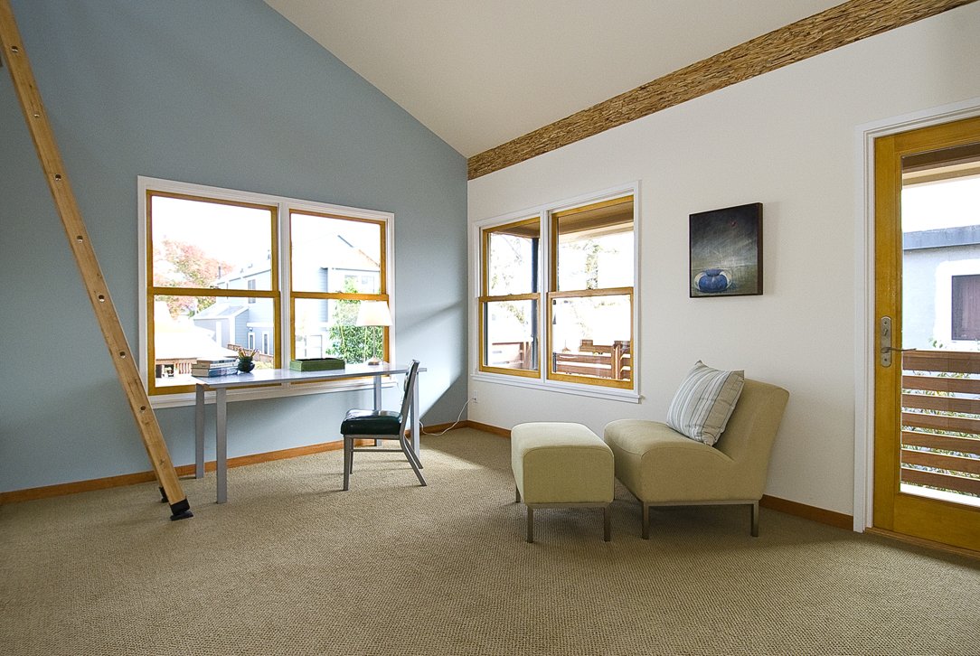 Bedroom sitting area with desk, lounge chair, and large windows, creating a flexible retreat that supports work and relaxation within the sustainable home plan.