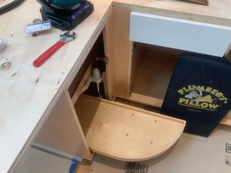Custom kitchen cabinetry under construction showing a curved pull-out shelf and plumbing access, illustrating Levitch’s detailed fabrication and storage planning.