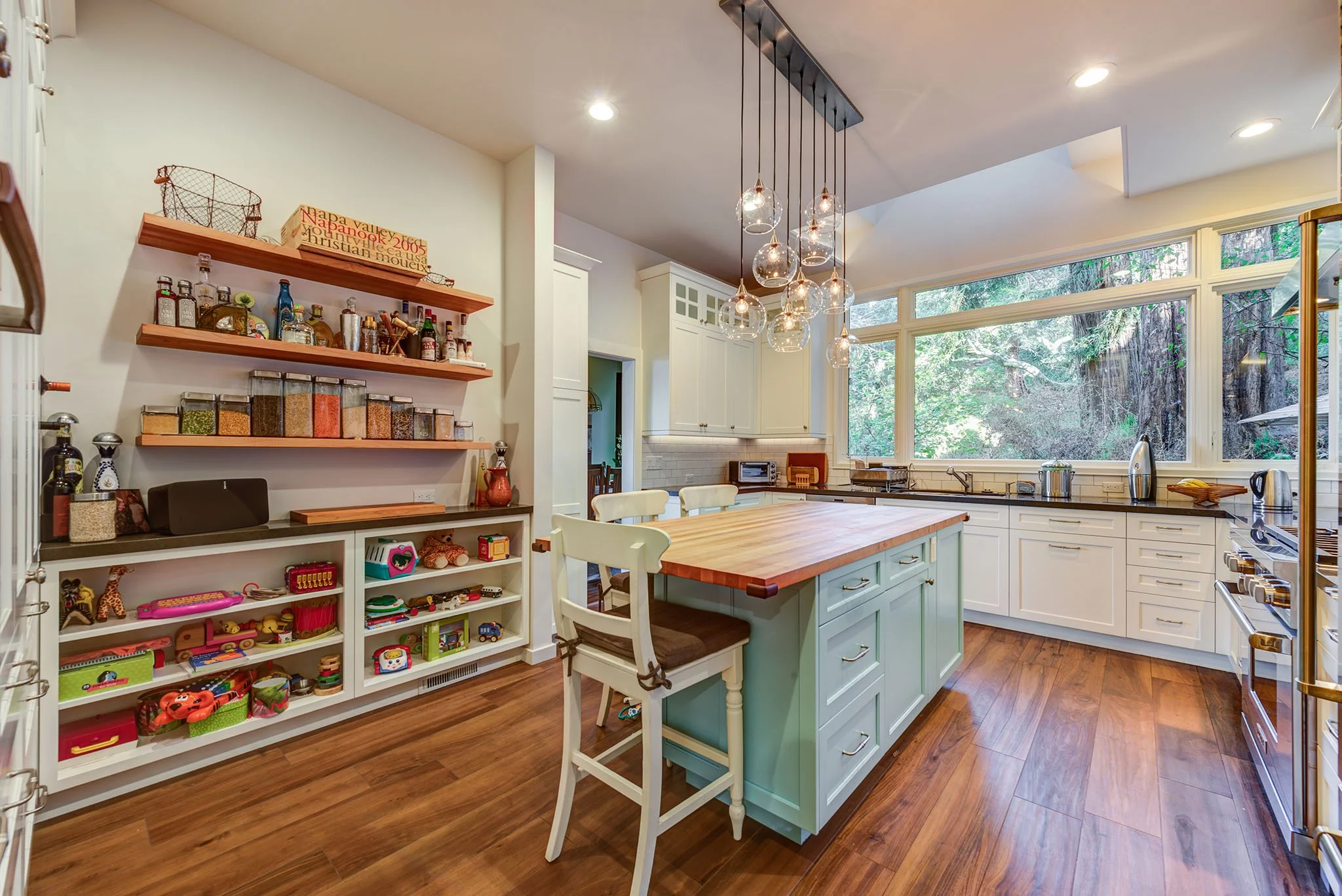 Kitchen remodel with painted cabinetry, butcher block island, open shelving, and large windows facing the trees, adding workspace for a growing family and home based business.