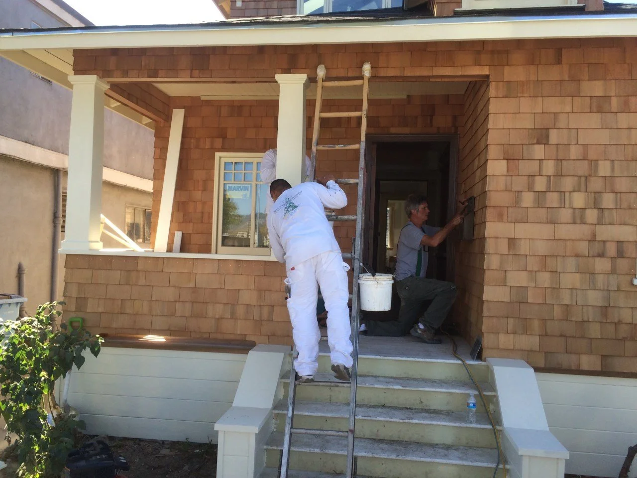 Carpenters install cedar shingles and trim at the front porch during the Craftsman renewal, updating the exterior while matching historic details and proportions.