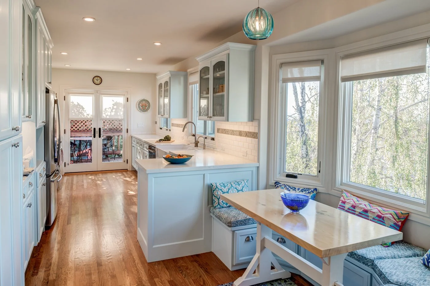 View from the breakfast nook into the updated galley kitchen, showing the straightened wall, new peninsula, bench seating, and doors that now open easily to the deck.