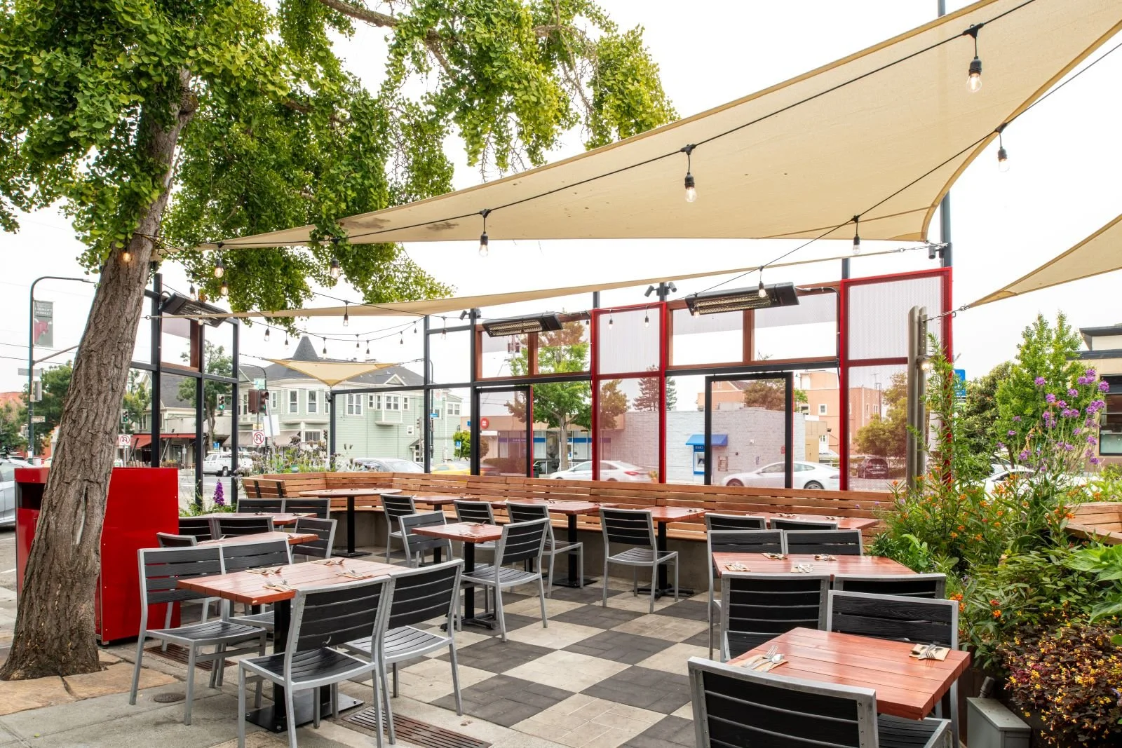 Full shot of Parklet showcasing the combination of fixed and moveable seating with shade sails and string lights overhead. 
