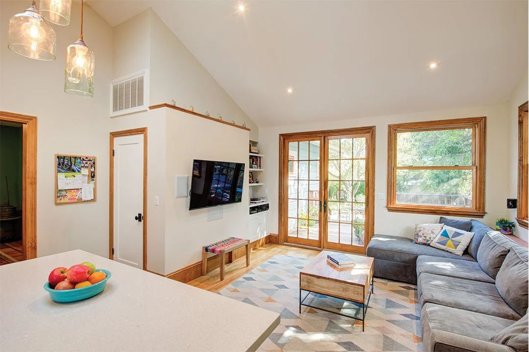 Family room with a vaulted ceiling and large windows, furnished for everyday living and positioned beside the kitchen for an open, shared family space.