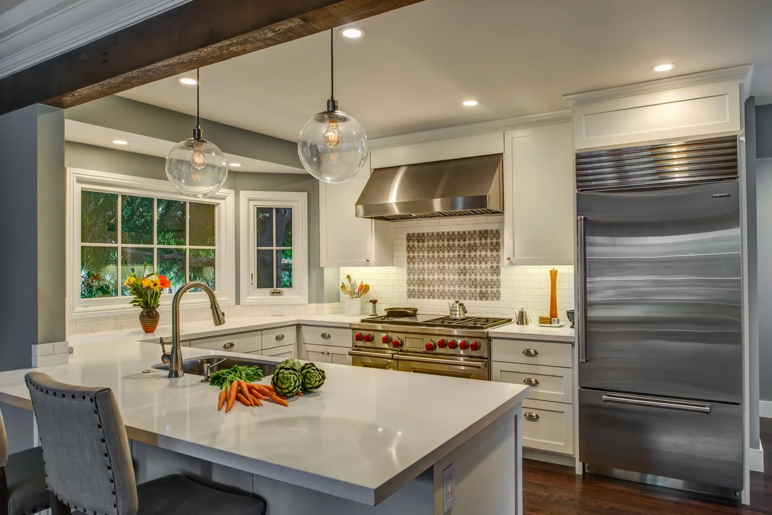 Remodeled kitchen with a large peninsula, ample white cabinetry, stainless range and hood, and windows over the counters, designed by Levitch for easier circulation and entertaining.
