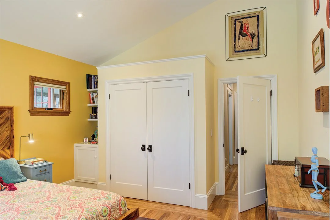 Bedroom with warm yellow walls, wood flooring, built-in storage, and a closet, created as part of the home’s reconfigured layout for added functionality.