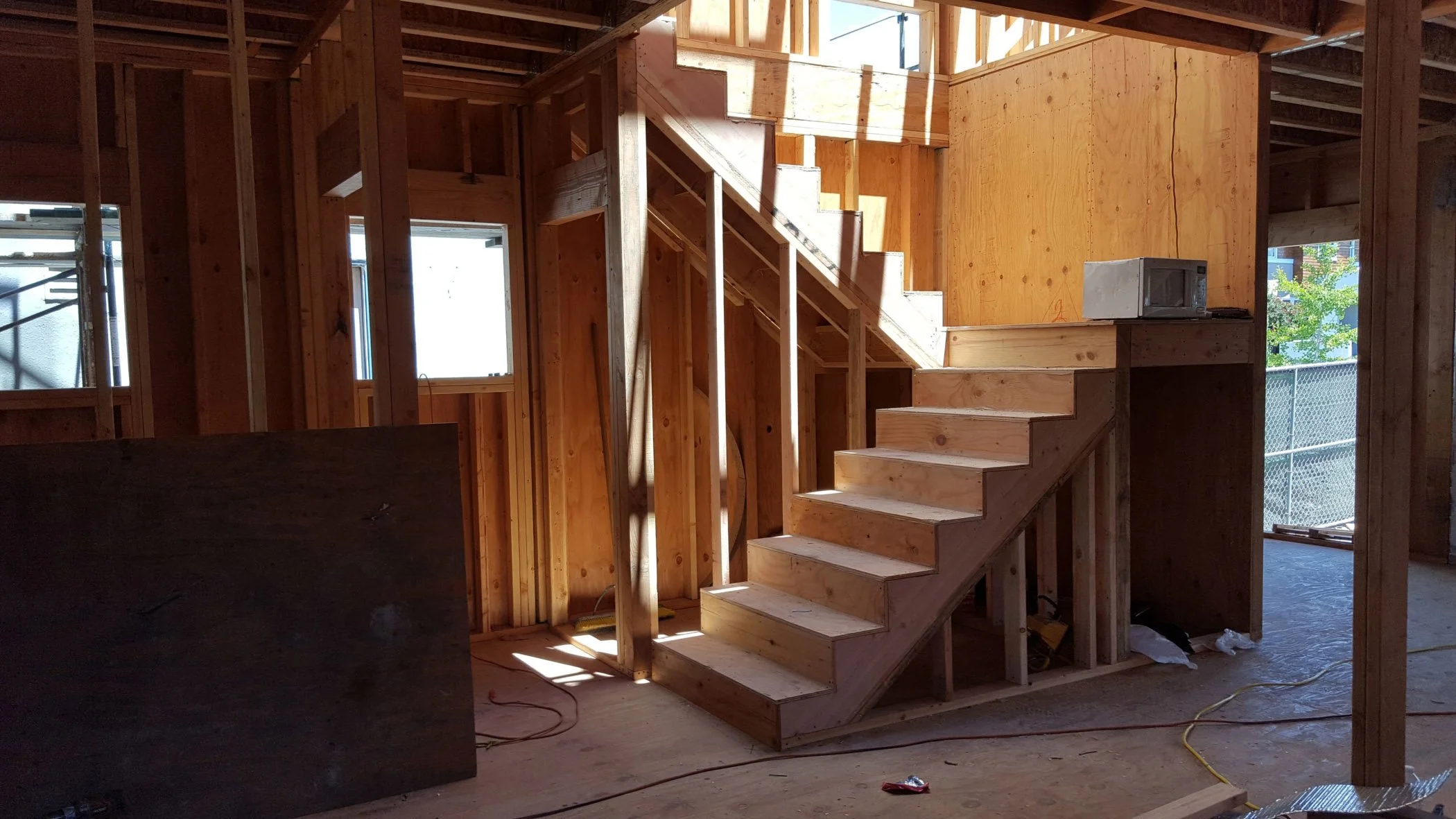 Staircase framing during the remodel, showing the compact stair run and landing under construction with exposed studs and daylight filtering in from new openings above.
