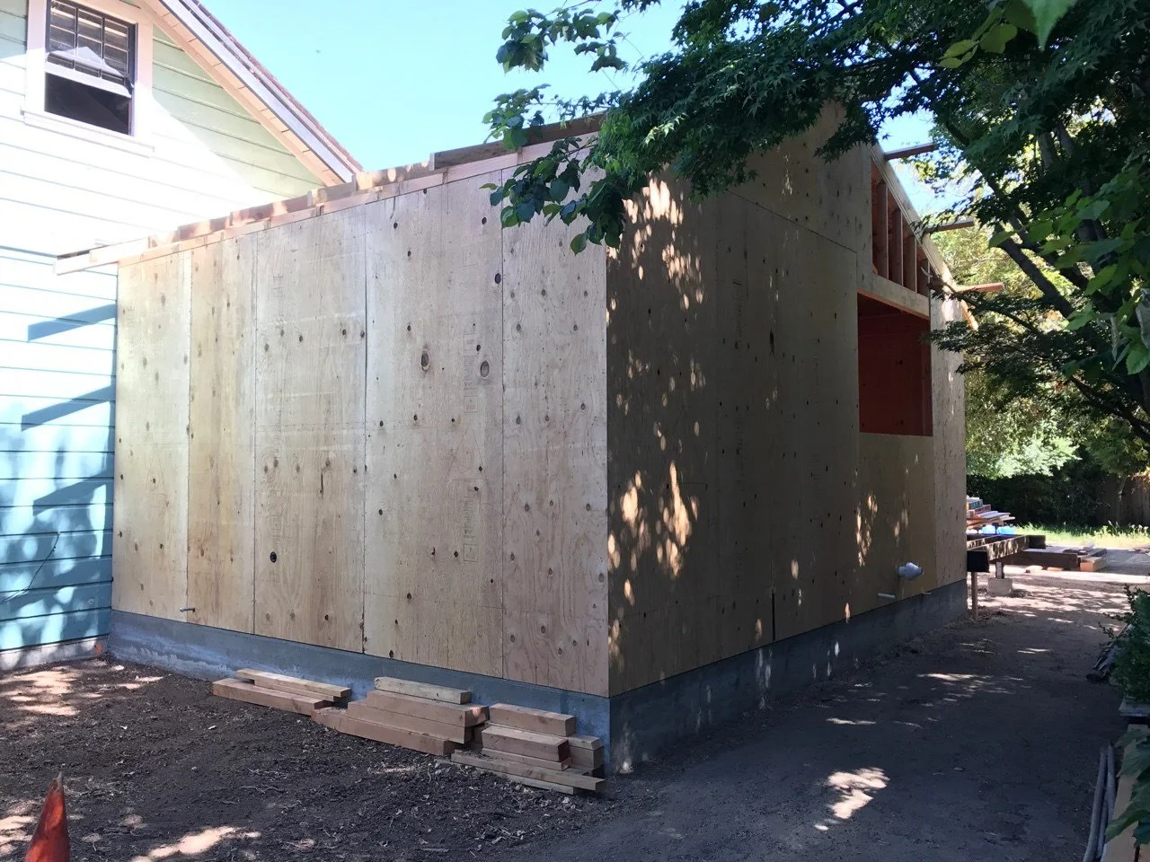 Exterior view of the home during construction, showing the new addition framed and sheathed, extending from the original structure before exterior finishes were installed.
