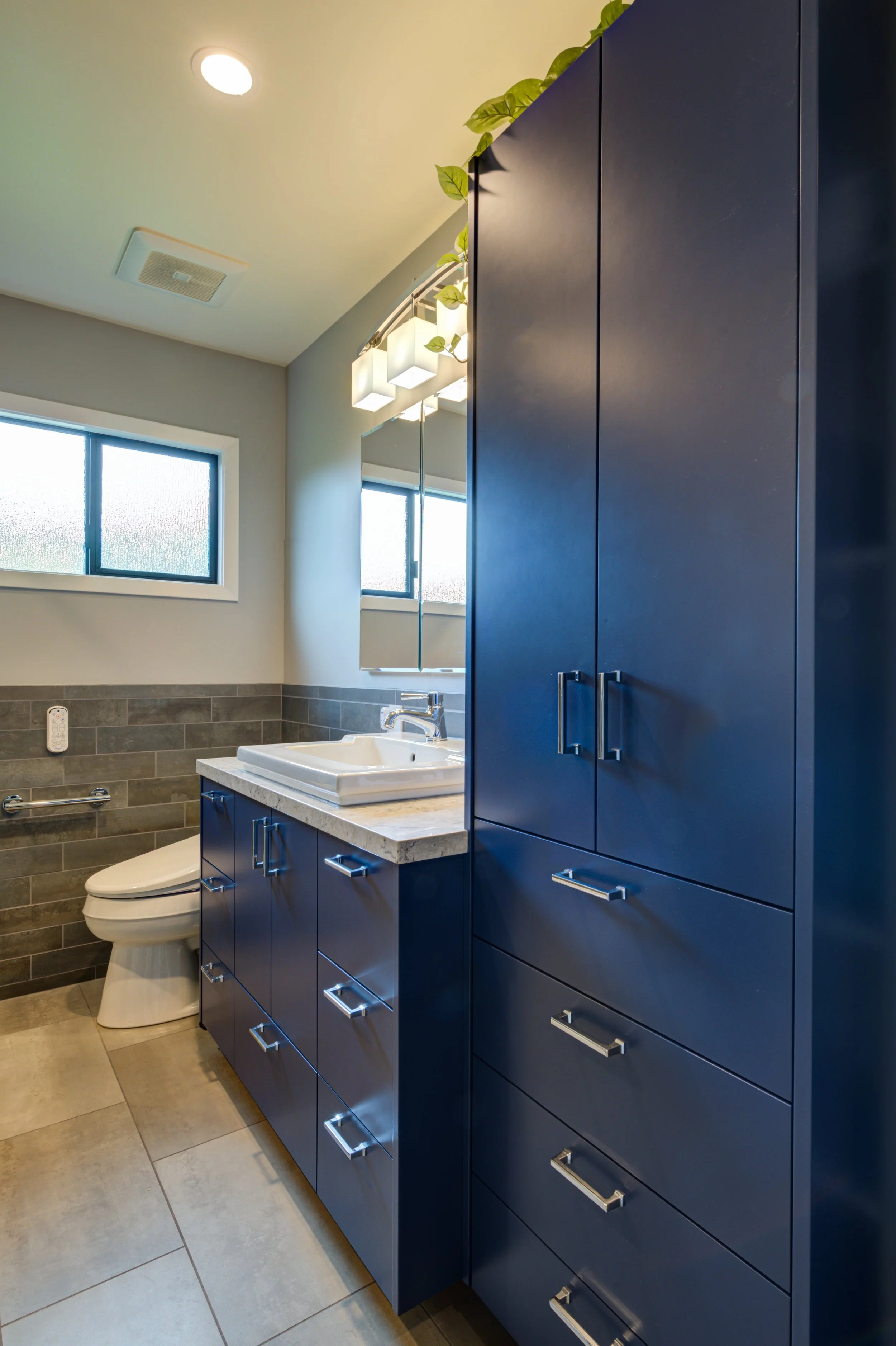 Modern bathroom with deep blue custom cabinetry, integrated storage tower, and a white vanity countertop, showing a clean and efficient layout designed for everyday residential use.