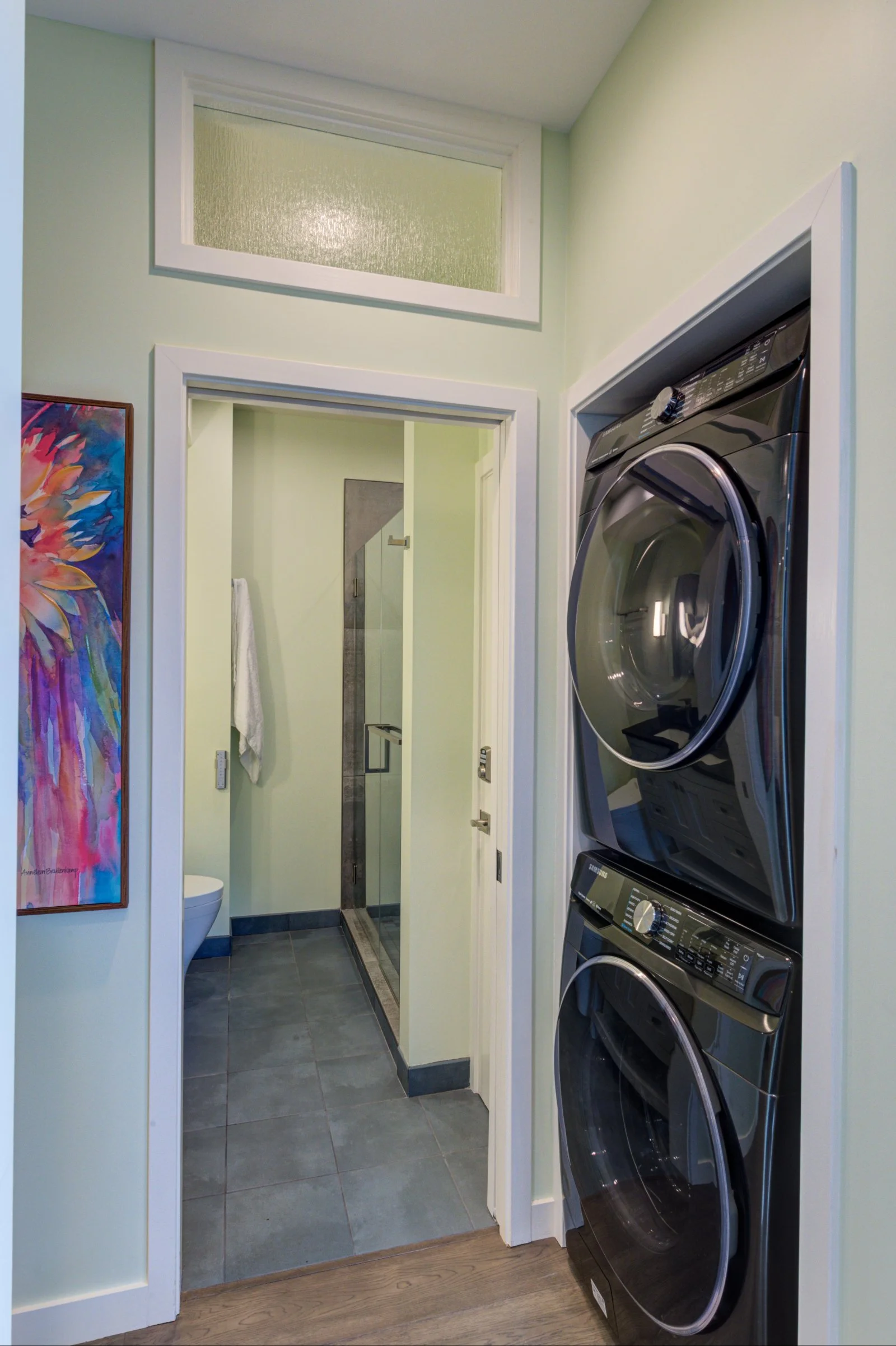 Hallway in Levitch’s Grand Lake ADU showing stacked washer and dryer, painted artwork, bathroom entry, clerestory window, and durable tile flooring.