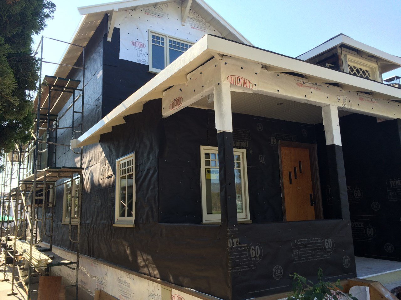 Home wrapped in weather barrier with scaffolding during the two story addition, showing roof and window openings prepared for new siding and Craftsman trim.