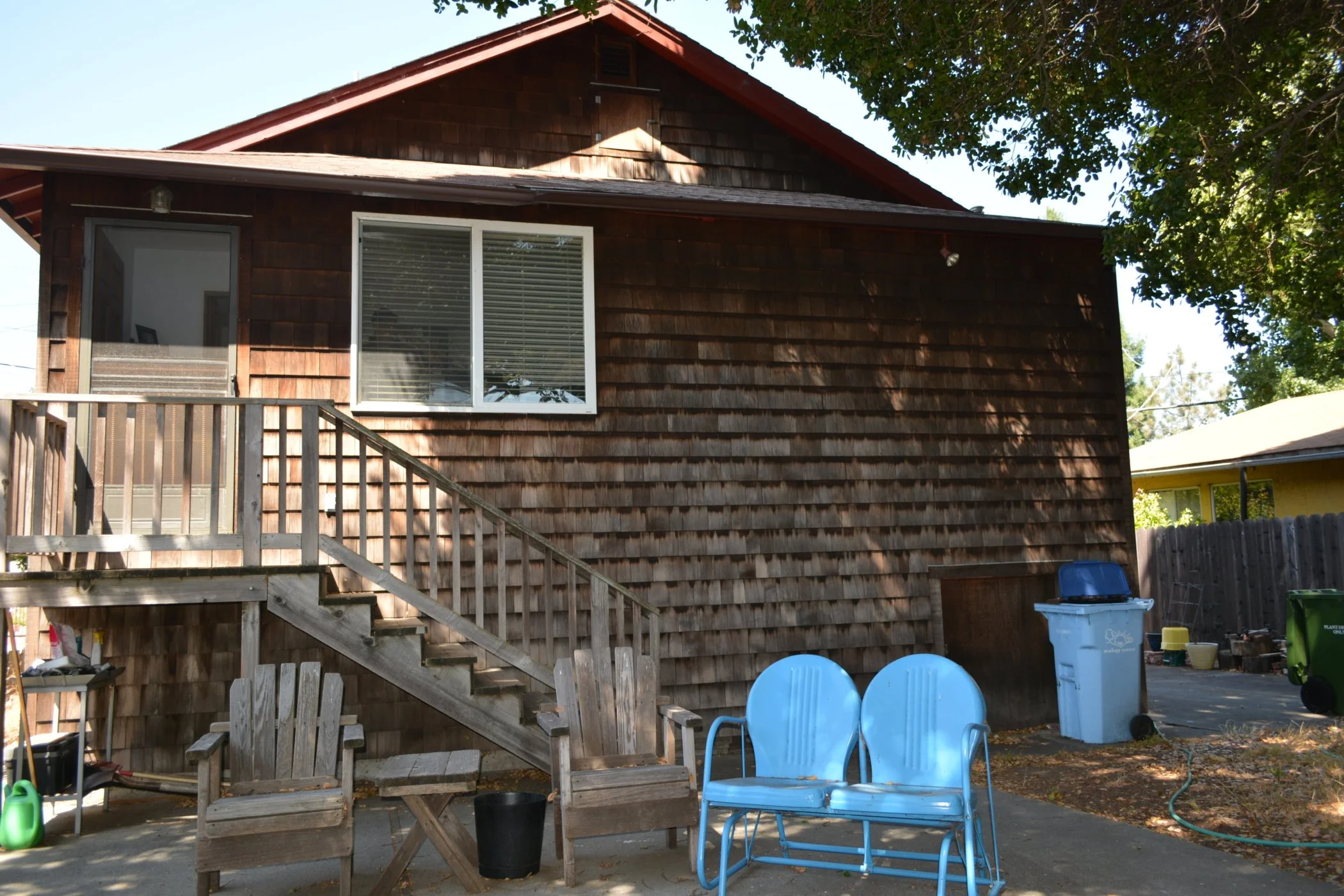 Back view of existing Berkeley home with wood shingle siding, aging stairs, and patio area prior to lift installation and structural renovation.