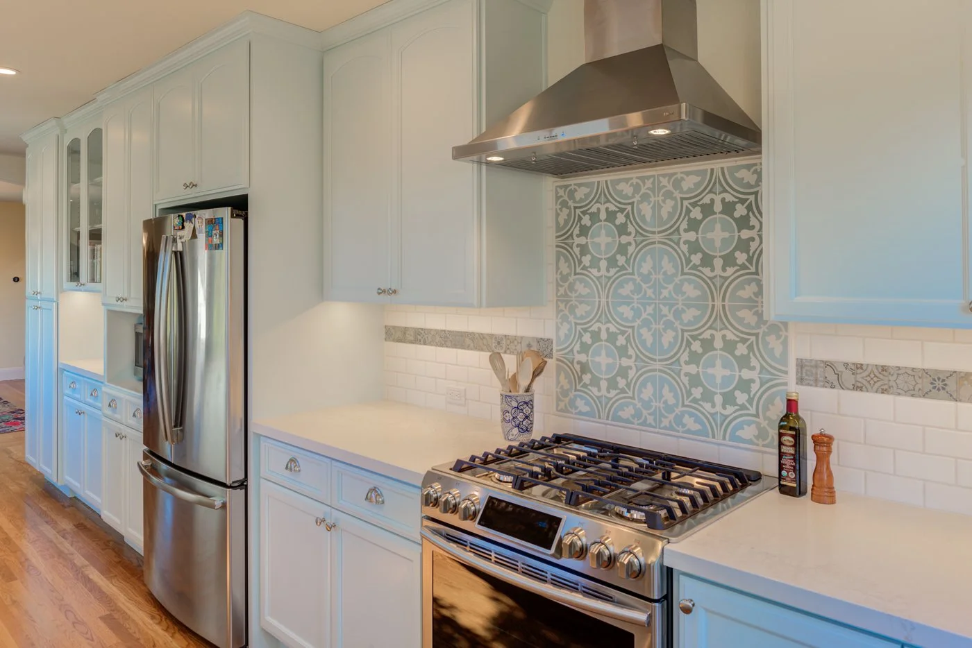 Remodeled kitchen range wall with light blue cabinetry, stainless hood and stove, and a decorative patterned tile accent framed by white subway tile backsplash.