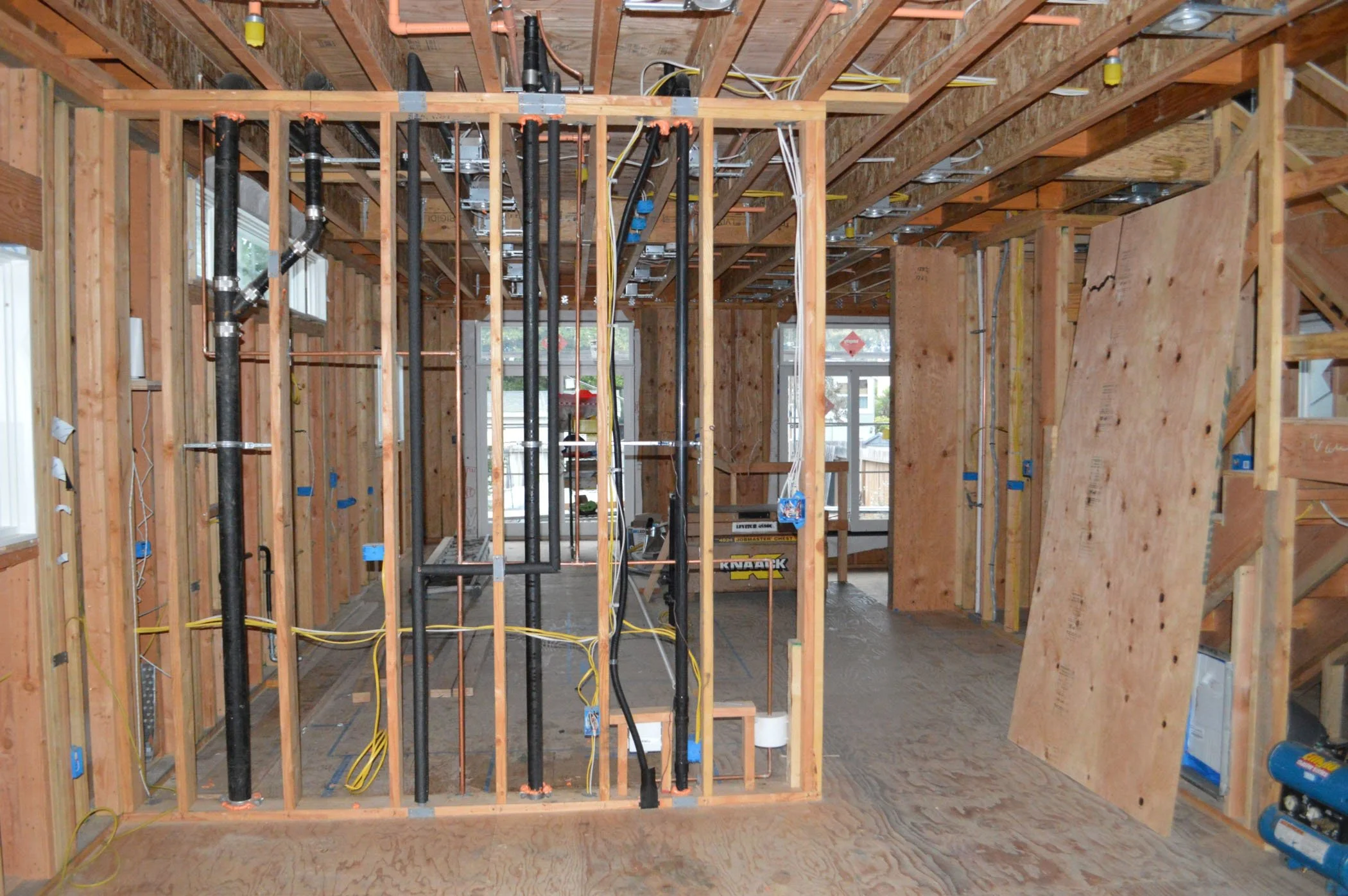 Main floor during construction, taken down to studs with exposed framing, plumbing, and electrical rough-ins, showing how the remodel opened up the plan before new finishes were installed.