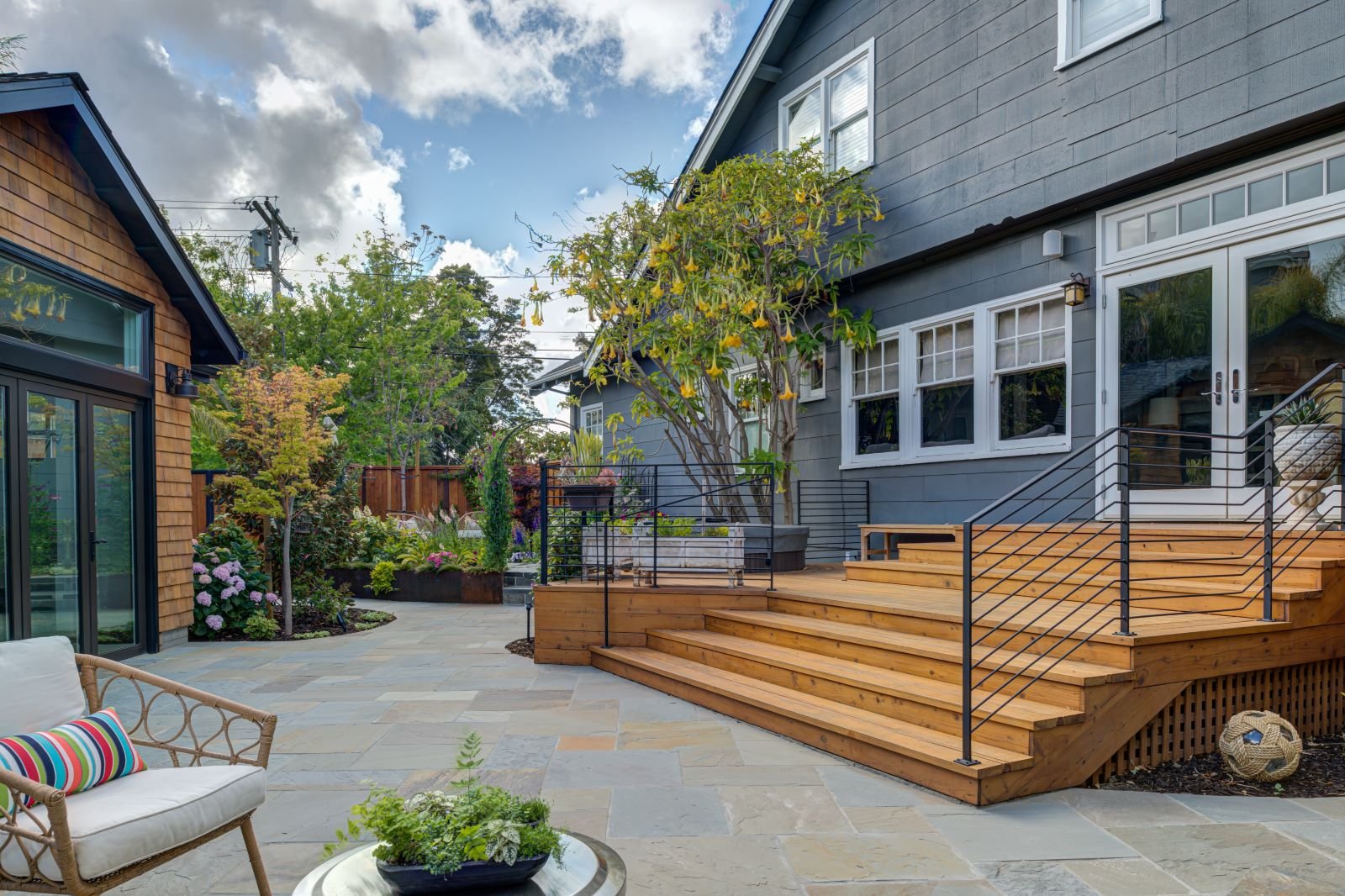 Entry terrace connects the main house to the accessory structure, using wood decking, steel railings, and stone paving to create a layered outdoor circulation space designed for gathering and transition.