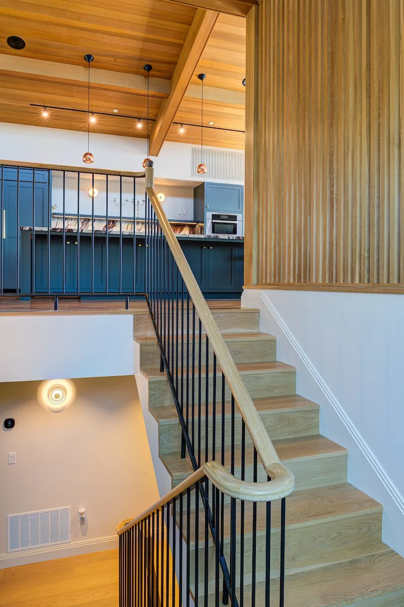 The open stair acts as a sculptural element within the living space, maintaining visual continuity between levels while connecting directly to the Kitchen.