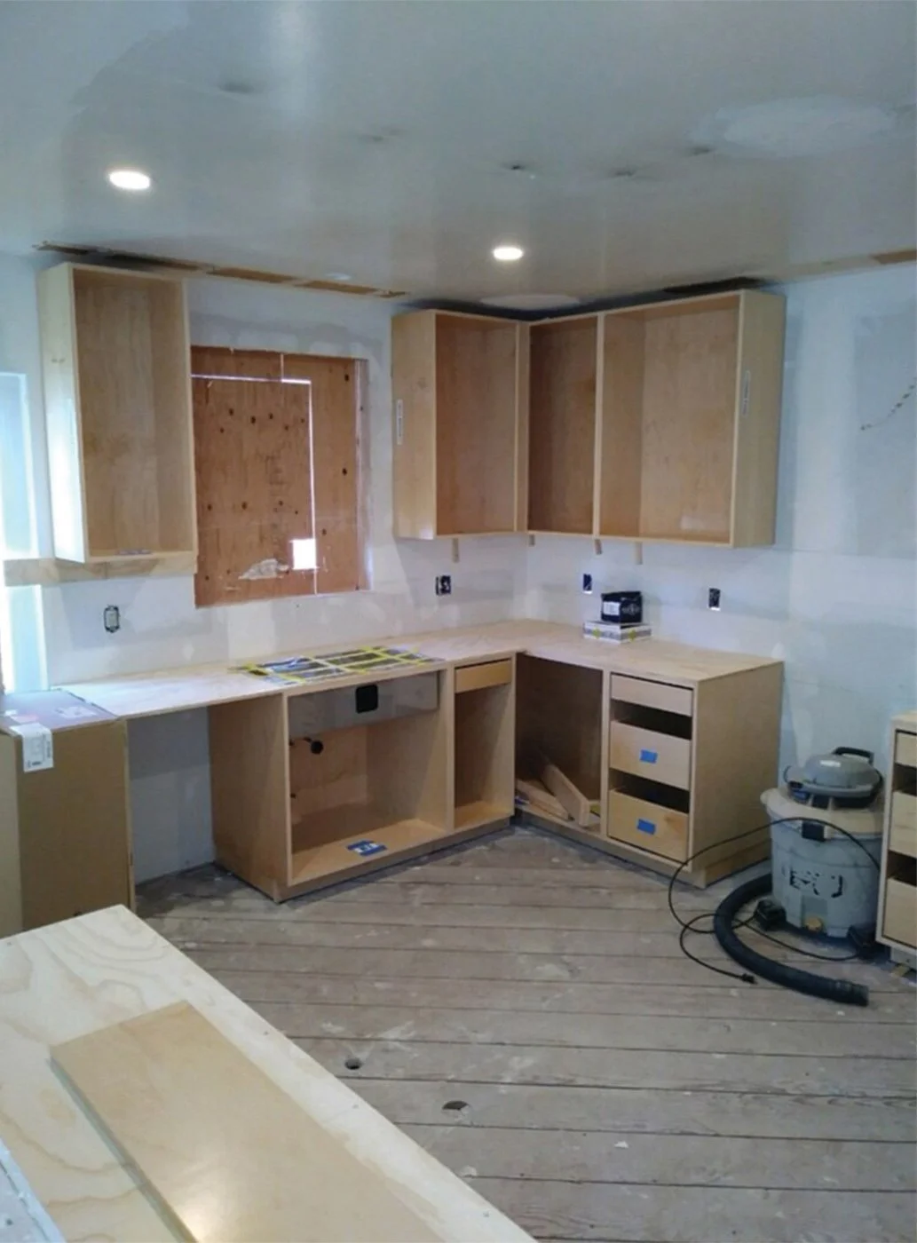 Kitchen during construction with unfinished cabinet boxes in place, taped seams and recessed lights overhead, and a shop vac on subflooring as Levitch builds the new layout.