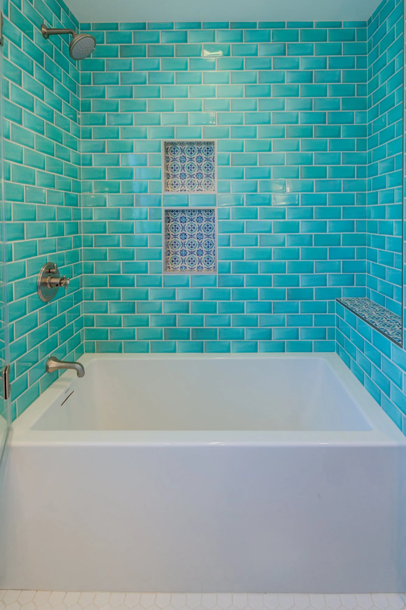 Bathtub and shower alcove finished with turquoise tile walls, patterned accent niches, and modern fixtures that reflect the colorful character of the remodel.