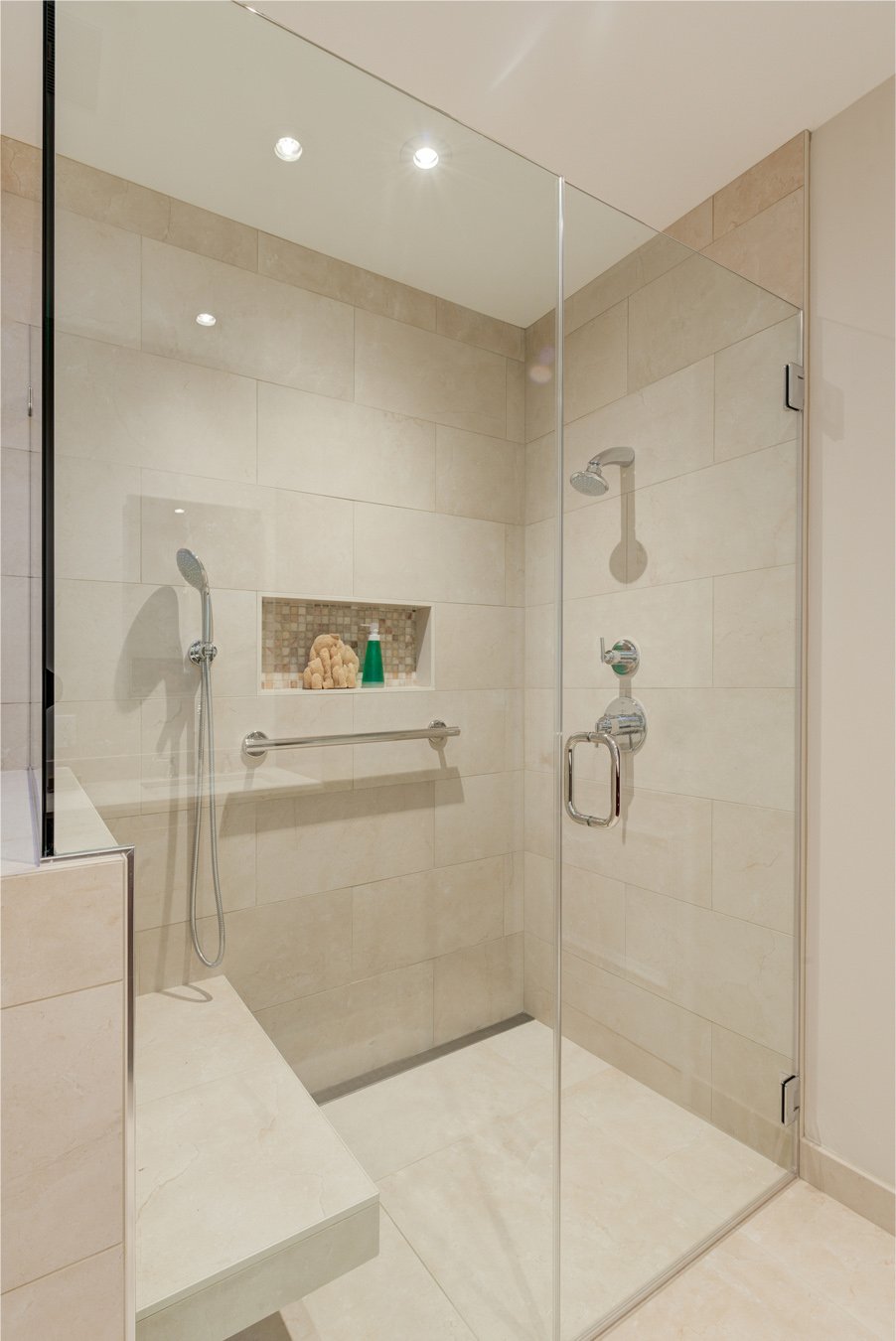 Levitch primary bathroom remodel in El Cerrito with large glass shower, built in bench, handheld and rain shower-heads, mosaic niche, and grab bar in warm neutral tile.
