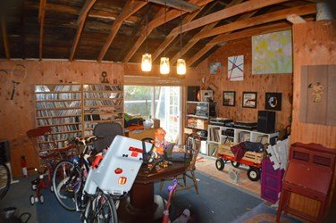 Original garage interior before renovation, with exposed framing, storage items, and low lighting, showing the starting condition prior to the Lighthearted home transformation.