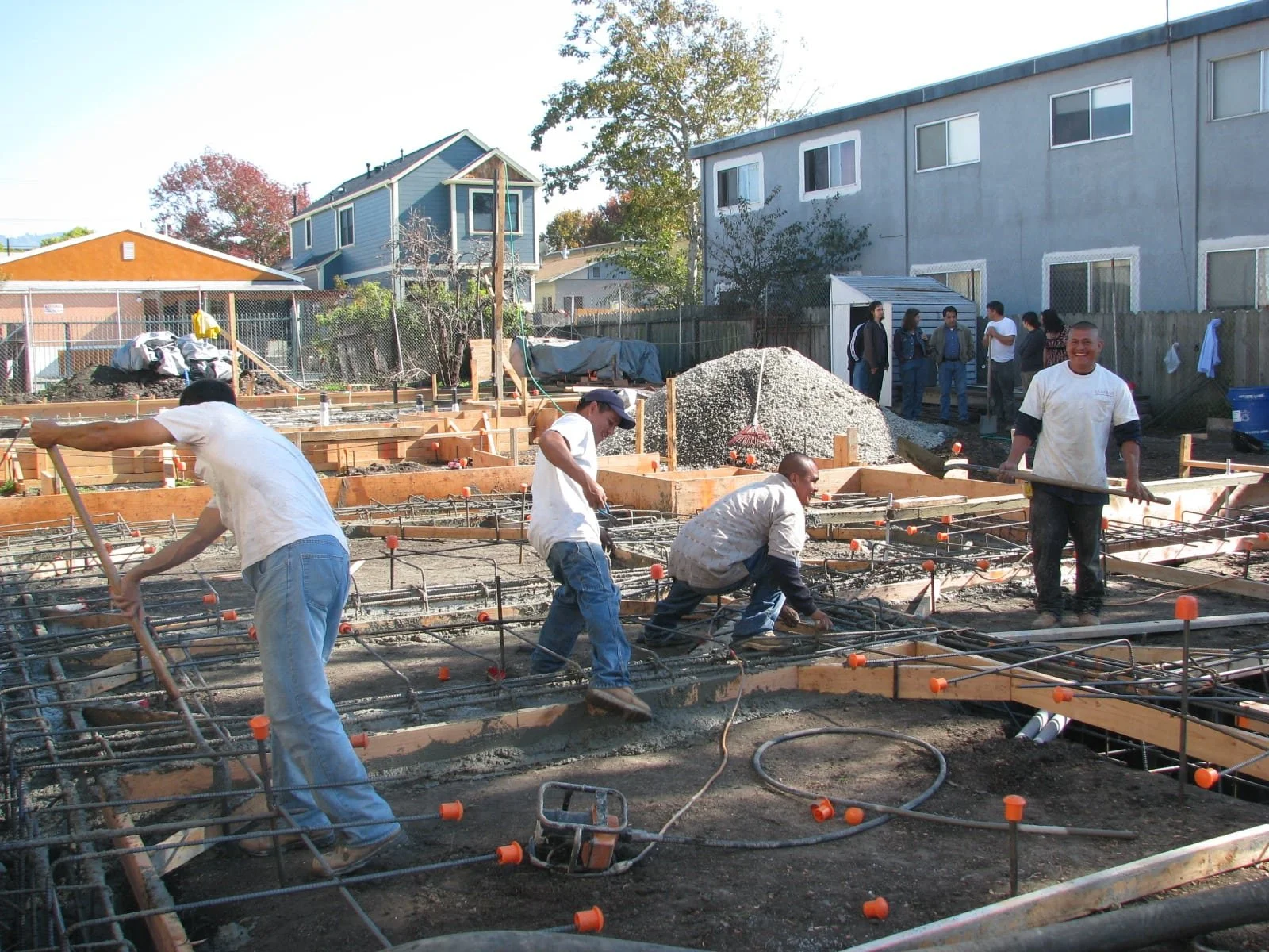 Workers pouring concrete footings within wooden formwork and steel rebar, showing early foundation construction for the Green Development Project with on-site coordination and sustainable building practices underway.