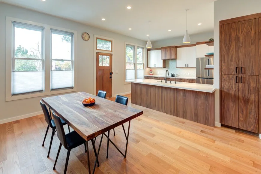 Open dining and kitchen area with built in walnut cabinetry, large peninsula, and expanded windows, creating a bright and flexible gathering space that makes the smaller home feel larger.