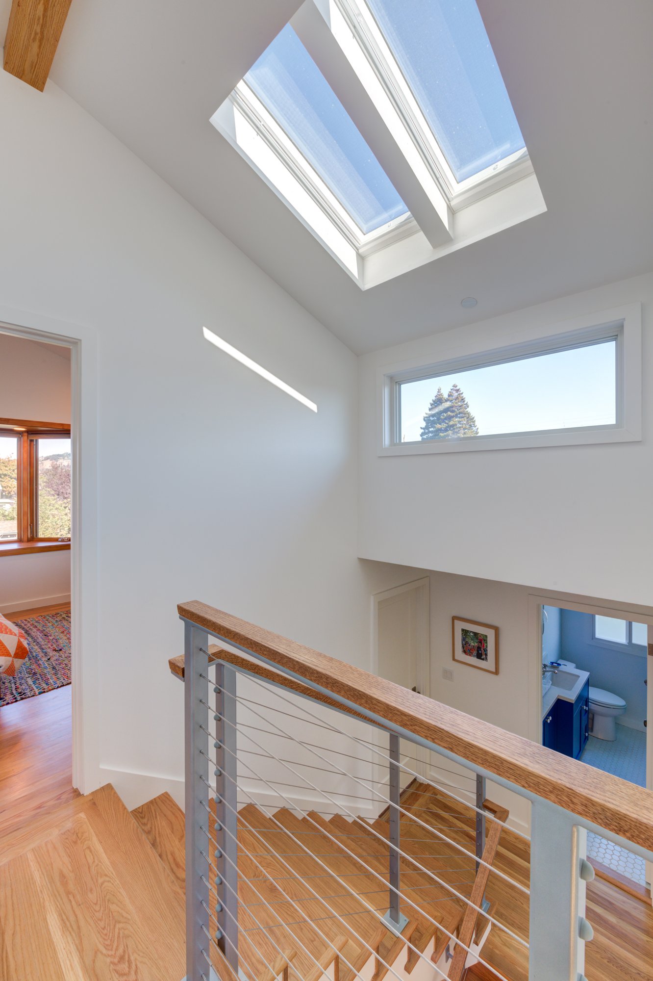 Upper landing with custom stair railing, wood treads, and cable guard, illuminated by two skylights and clerestory windows that bring natural light into the second-story addition.
