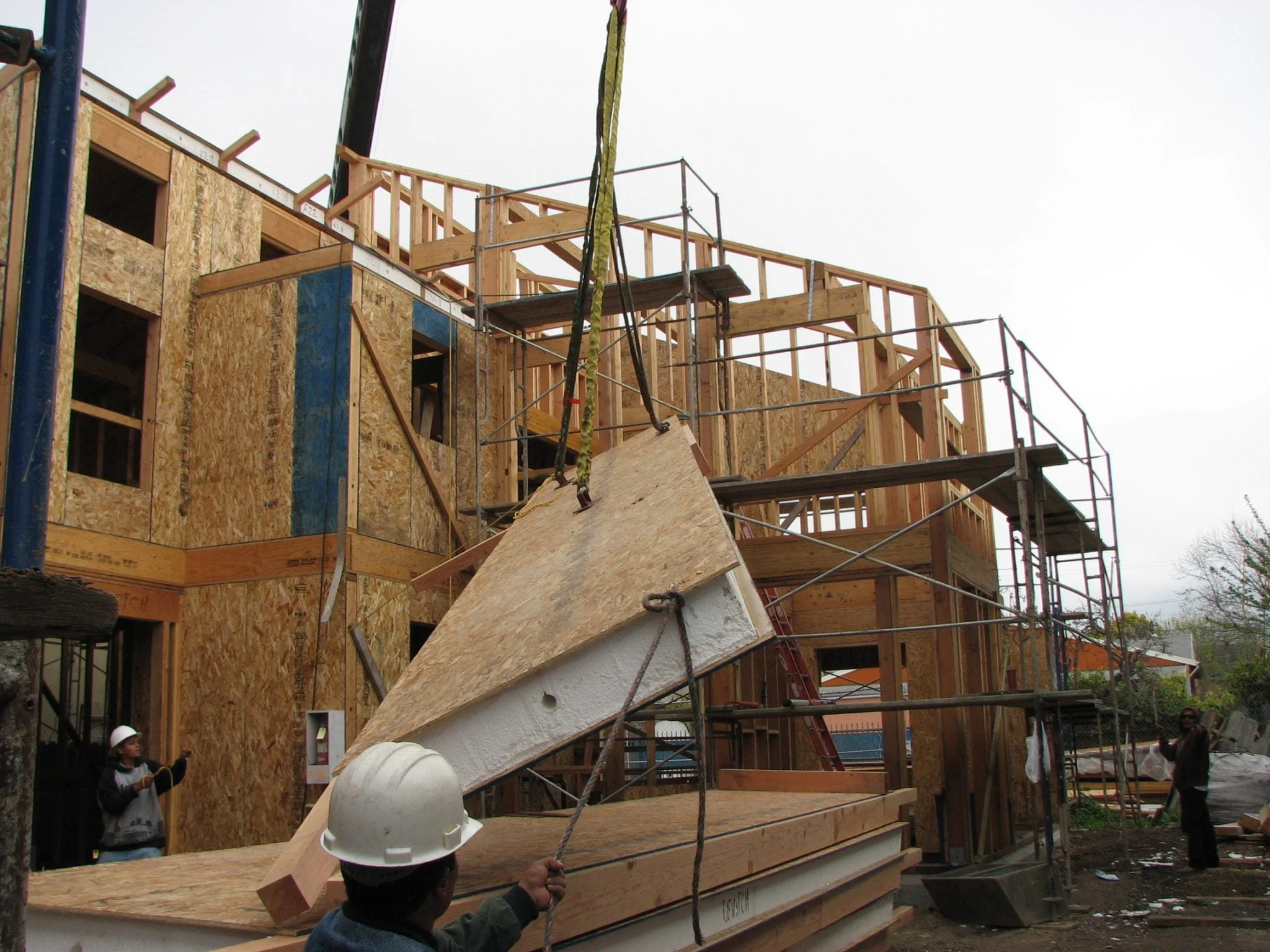 Prefabricated insulated wall panel being craned into place during framing, illustrating efficient construction methods and material reuse that support the Green Development Project’s sustainability goals.