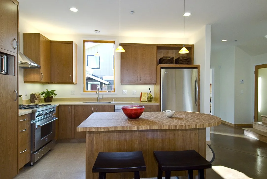 Kitchen view from the central island toward the sink wall, highlighting custom wood cabinetry, efficient work zones, and daylight focused layout in the open plan design.