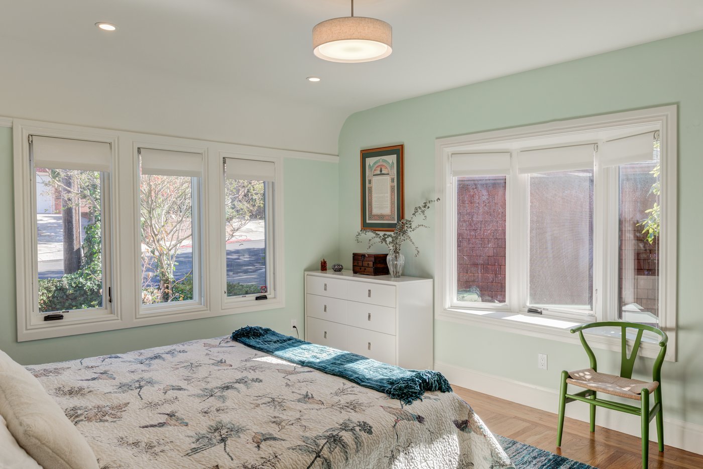 Newly finished bedroom with soft green walls, added windows for daylight, and simple furnishings, part of the larger remodel that created more functional living space.